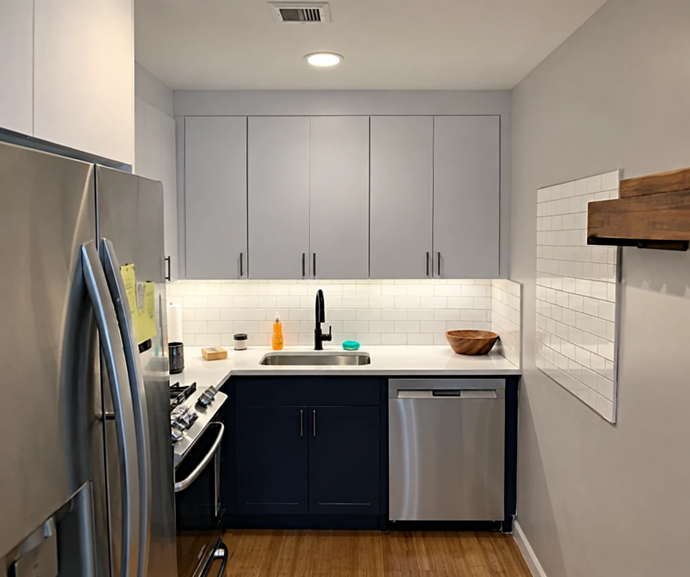 Compact kitchen with a stainless steel refrigerator, white upper cabinets, and dishwasher