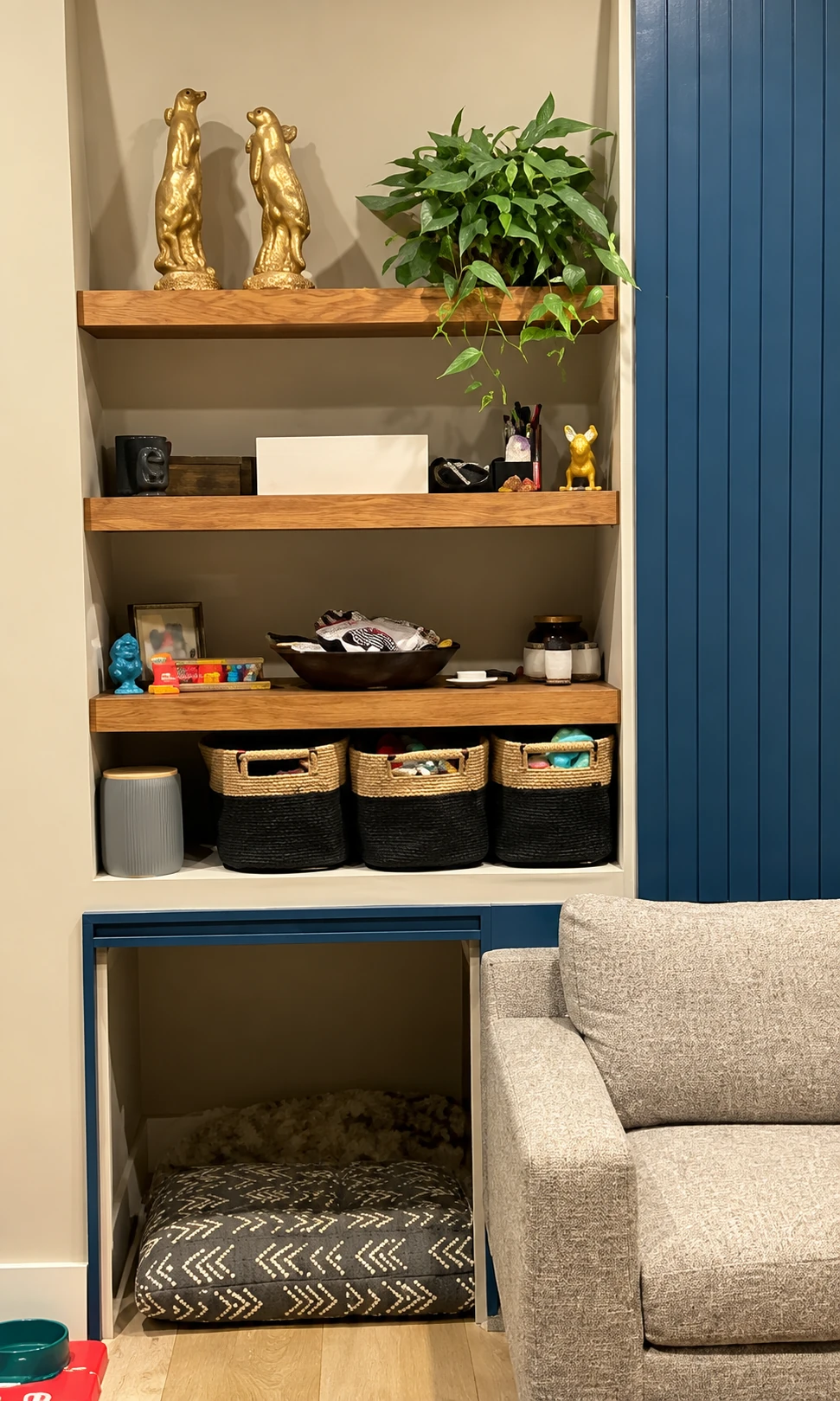 Built-in wood shelves with storage baskets and a pet nook beside a living room sofa