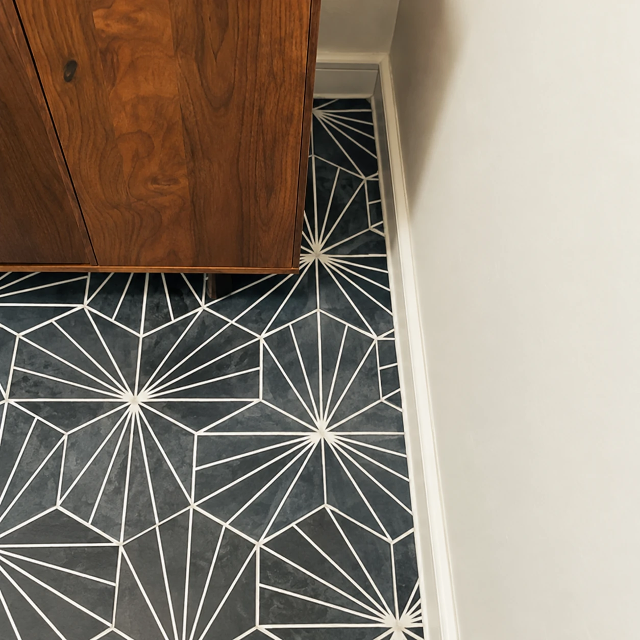 Detail of black and white geometric floor tiles along a wood vanity and white wall