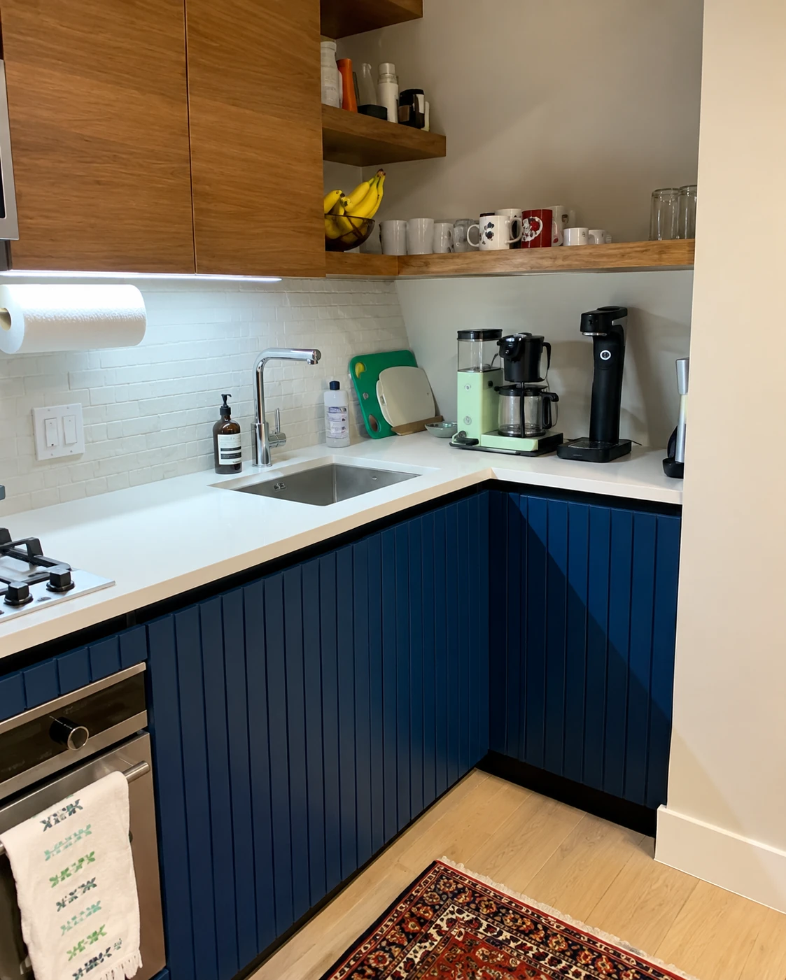 L-shaped kitchen with blue cabinets, a white countertop, and wood shelves