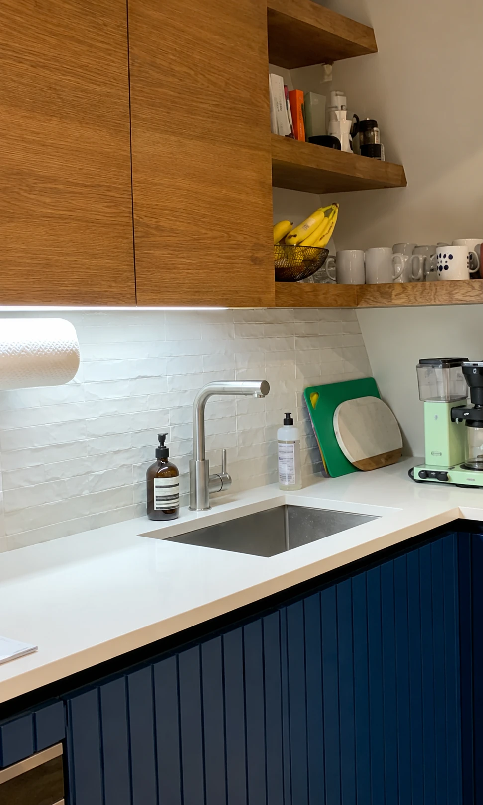 Kitchen sink with a white backsplash, blue lower cabinets, and wood shelves
