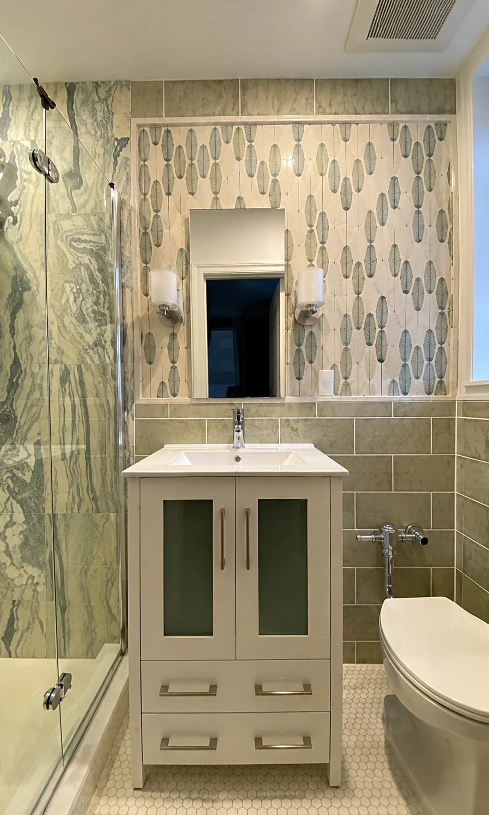 Bathroom with a white vanity, botanical wallpaper, and glass shower enclosure