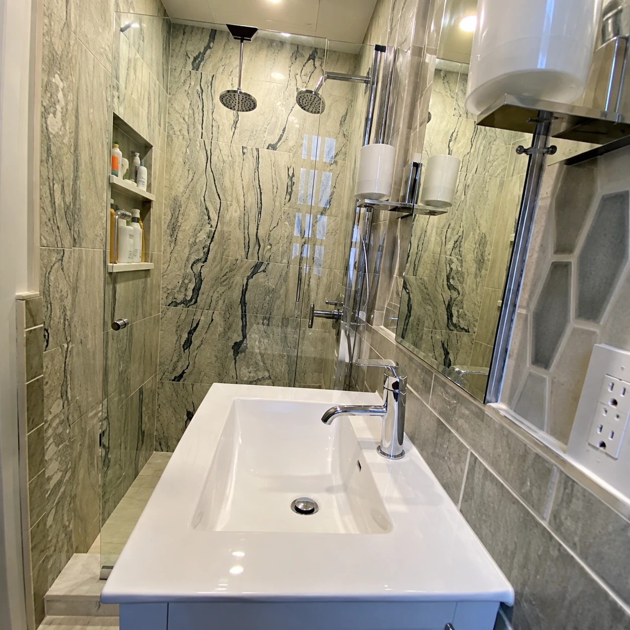 Compact bathroom with a white vanity, glass shower enclosure, and veined shower tiles