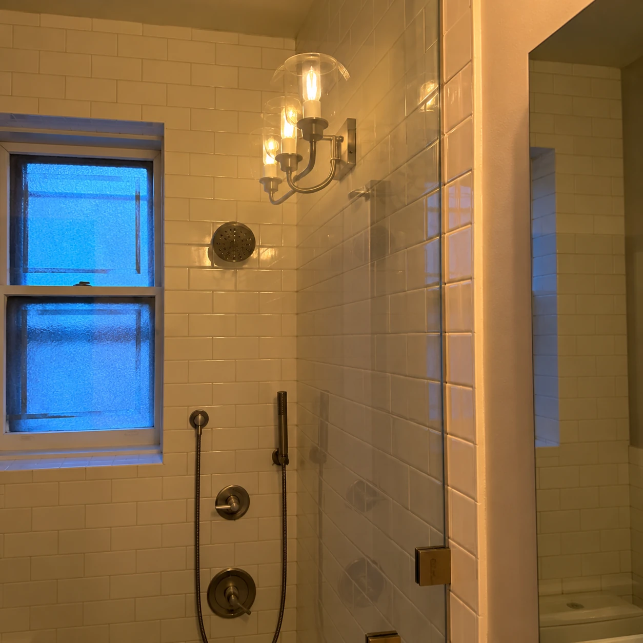 Glass shower enclosure with white subway tiles and a bathroom window